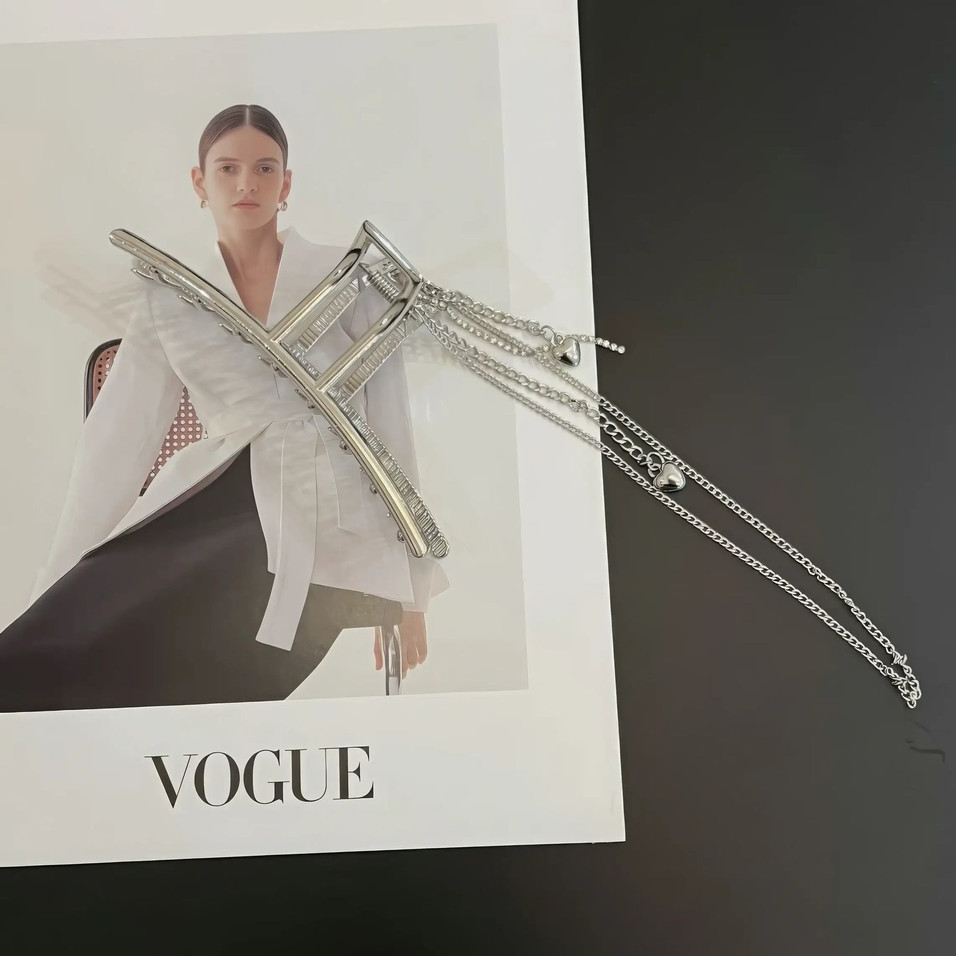 Silver heart - shaped tassel chain hair claw placed with "VOGUE" magazine, highlighting style