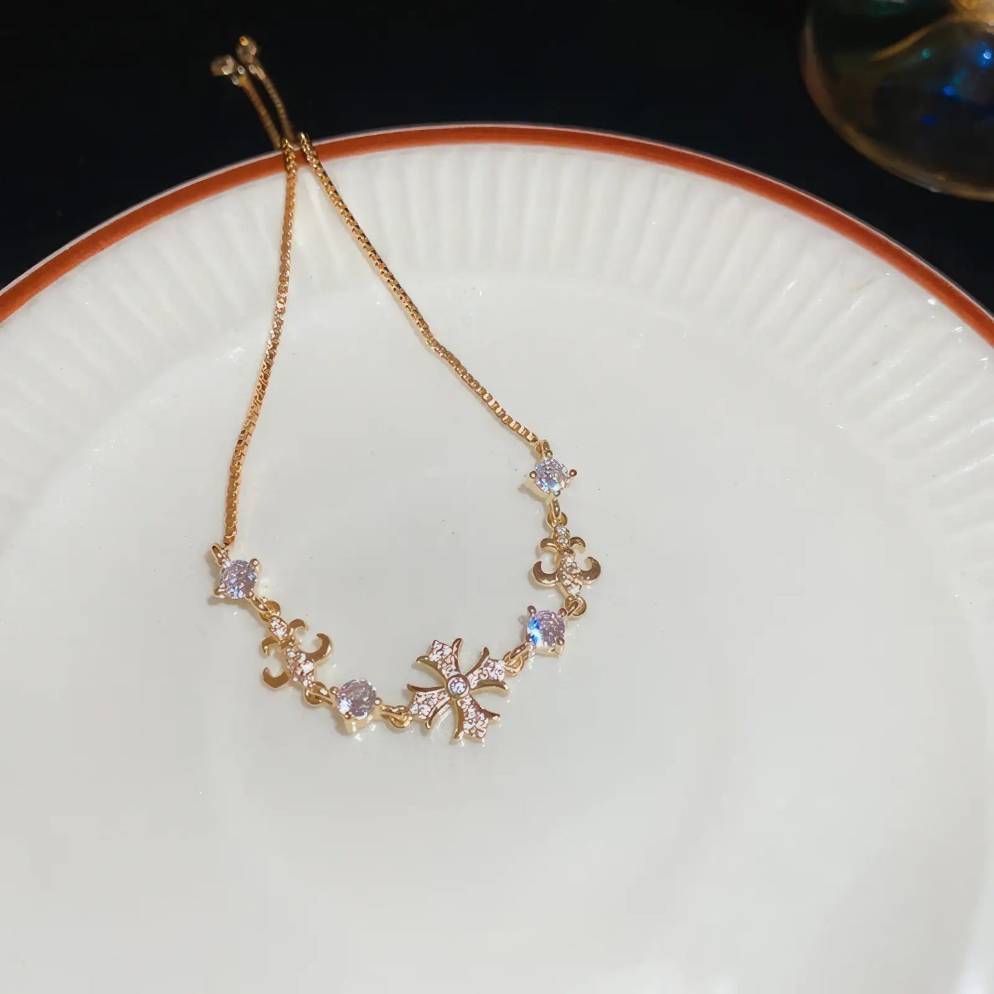 Iris cross bracelet, gold - tone, displayed on white plate