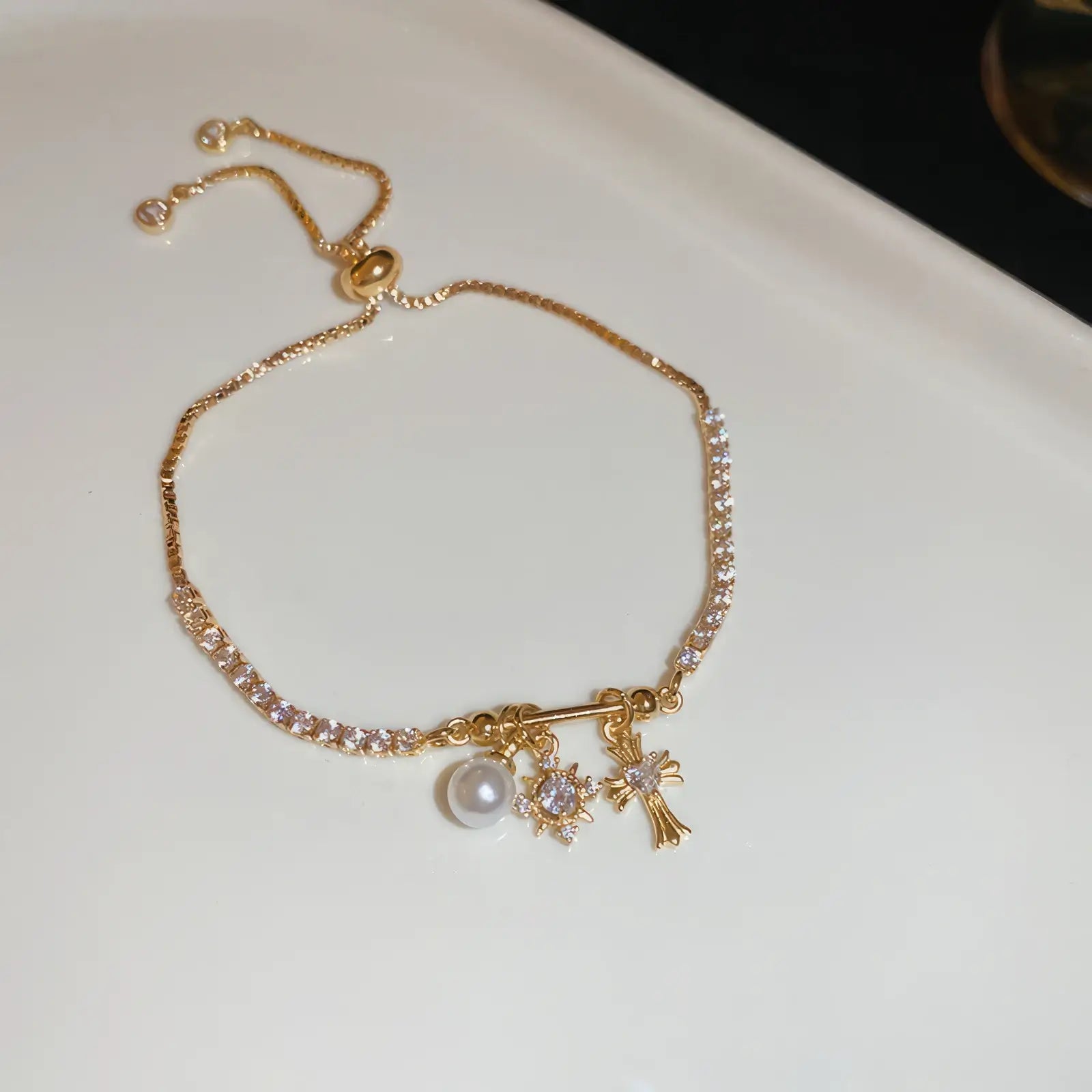 Iris cross bracelet with pearl, gold - tone, displayed on white pad