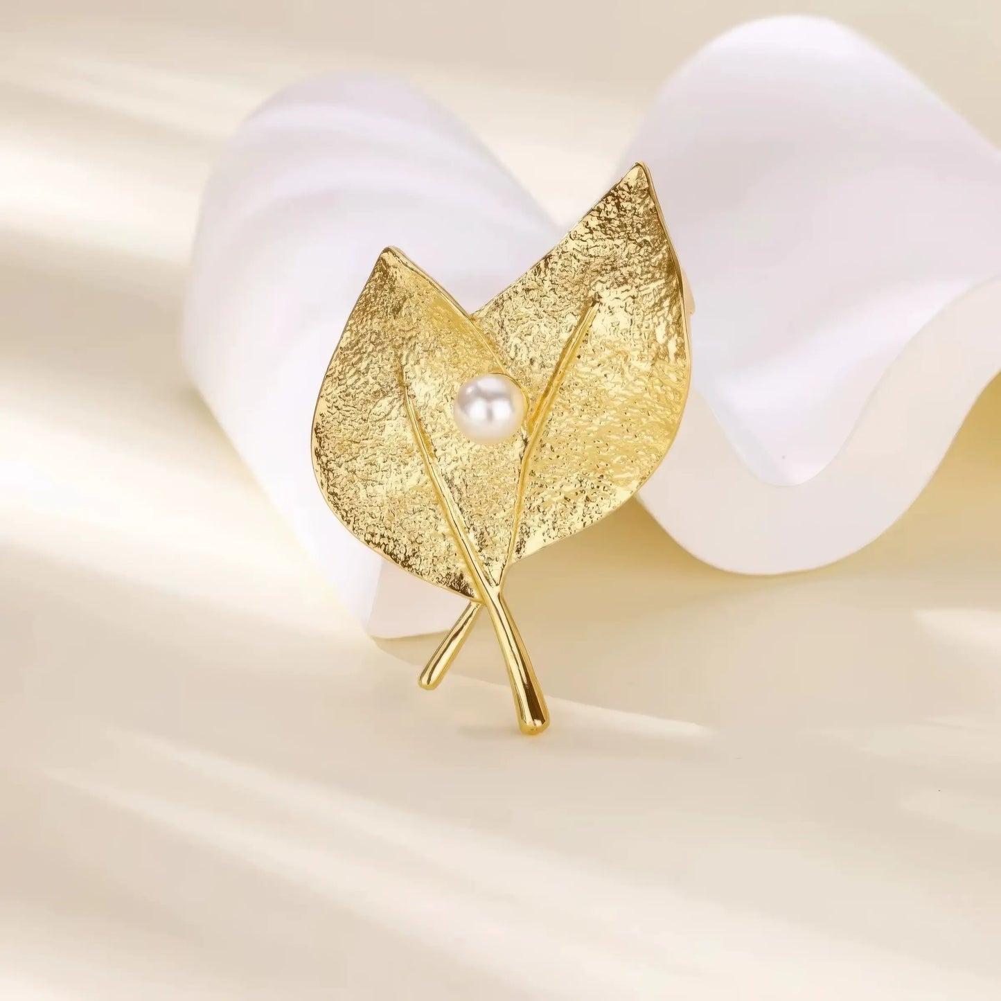 Gold leaf - shaped brooch with pearl, displayed with white petals, showcasing elegant design