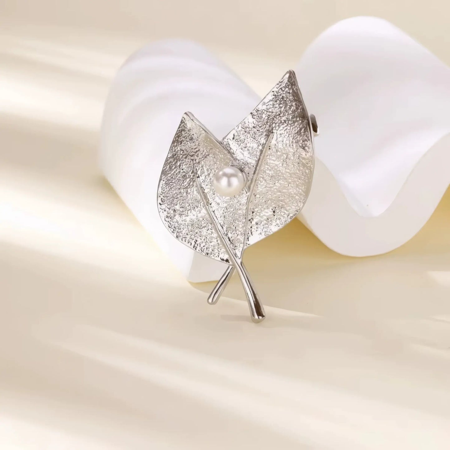 Silver leaf - shaped brooch with pearl, displayed with white petals, emphasizing delicate style