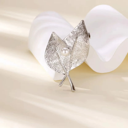 Silver leaf - shaped brooch with pearl, displayed with white petals, emphasizing delicate style