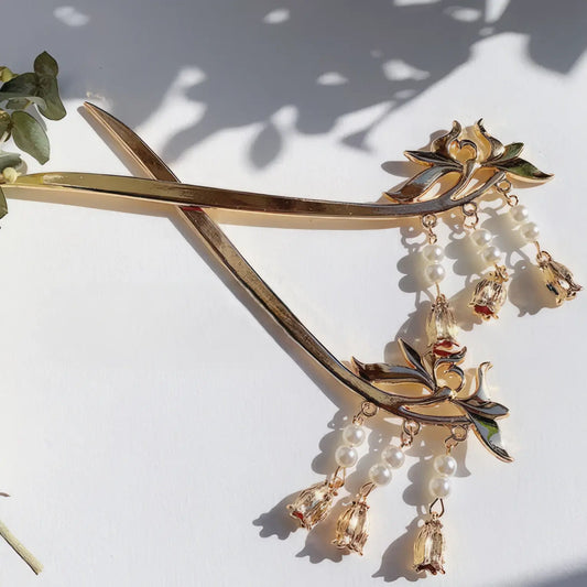 Lily - of - valley hairpin, gold with pearl tassels, against white background with greenery