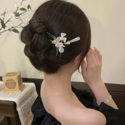 A woman with a bun wearing the magnolia hairpin while tidying it, in a black dress