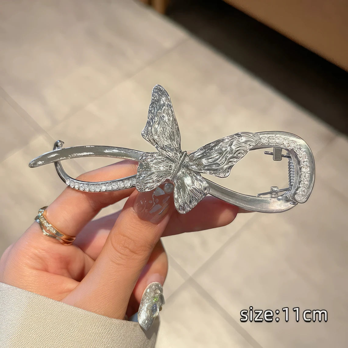 Hand holding silver metal butterfly twist clip, light surface background, size (11cm)