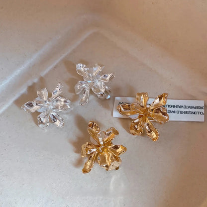 Mixed metal flower ear clips (silver and gold) displayed on a light surface with a card