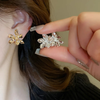 Mixed metal flower ear clips (silver and gold) worn, hand holding one ear clip, dark clothing background