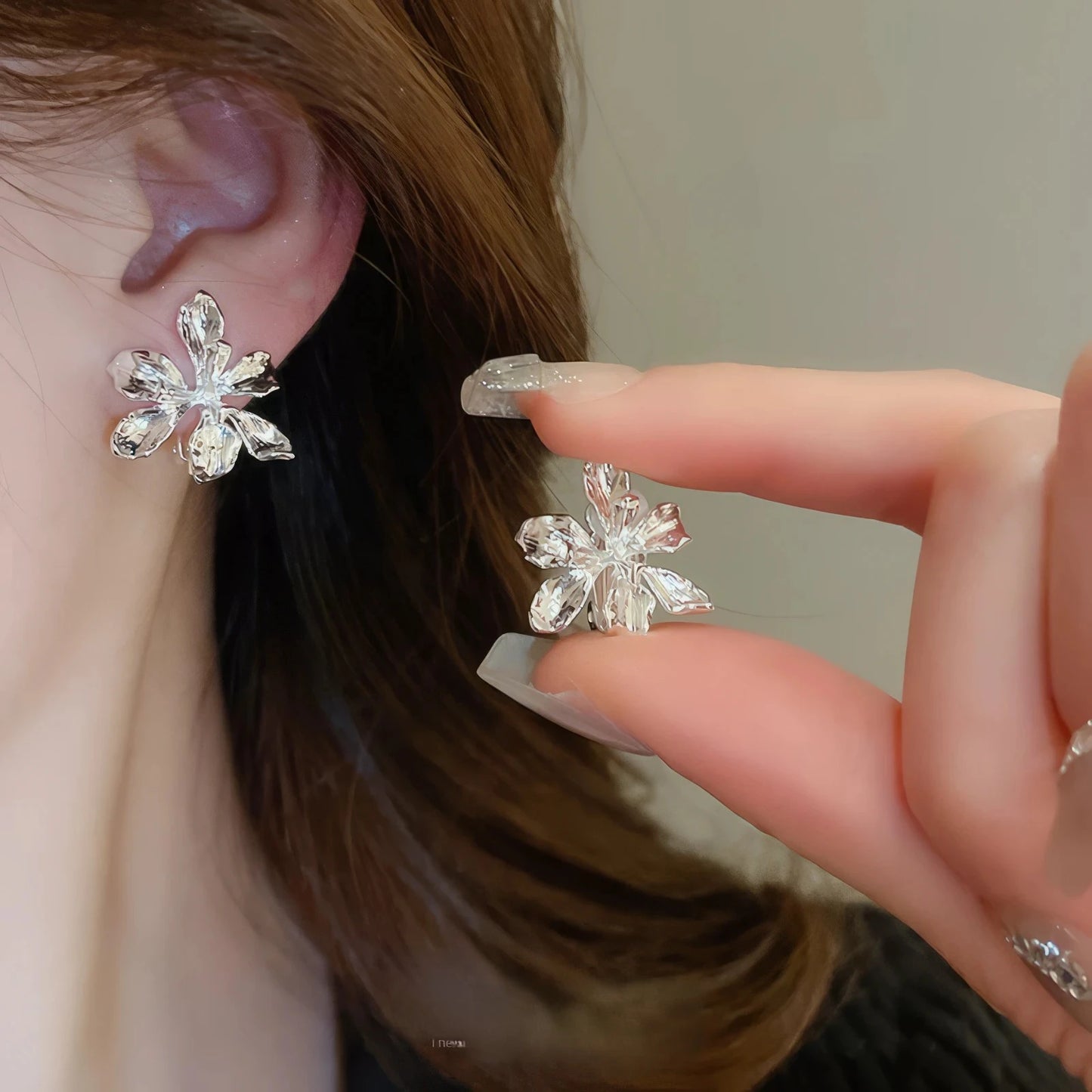Silver metal flower ear clips worn, hand holding one ear clip, dark clothing background