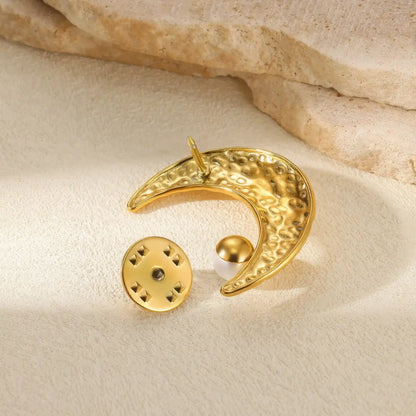 Back view of gold moon - shaped brooch with pearls, placed on beige fabric, emphasizing details
