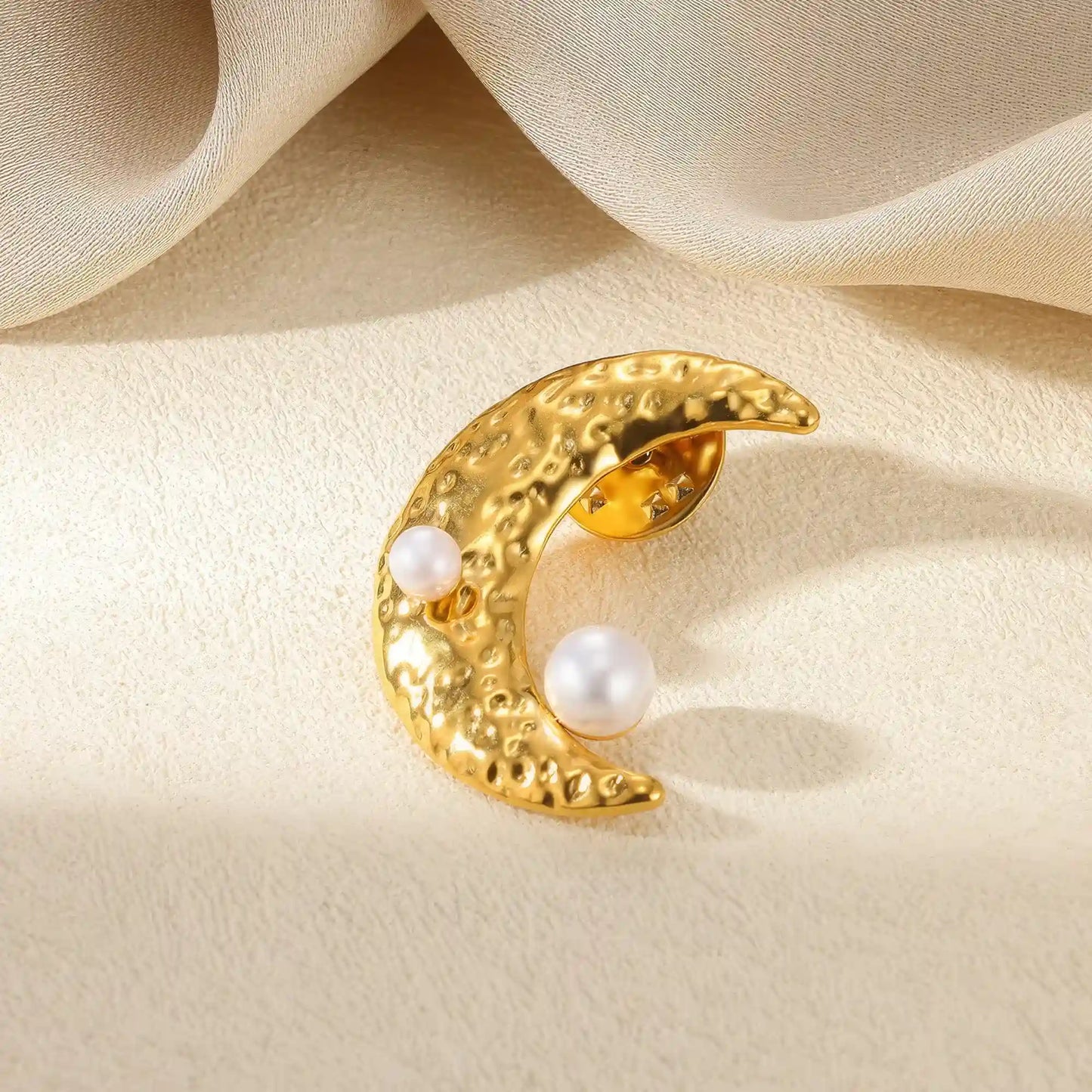 Gold moon - shaped brooch with pearls, placed on beige fabric, highlighting elegance
