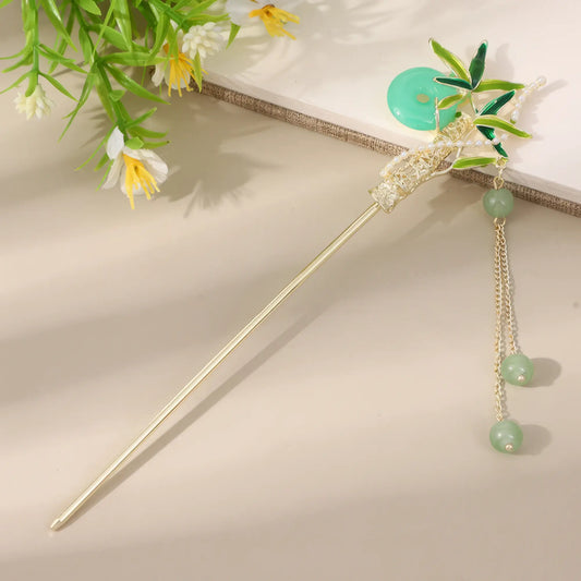 Moyunxuan hairpin, gold with green bead and tassel, on beige background with greenery