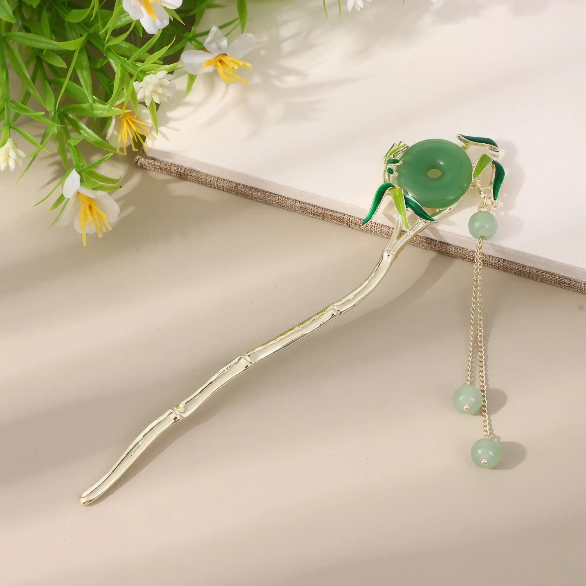 Moyunxuan hairpin, silver with green bead and tassel, on beige background with greenery