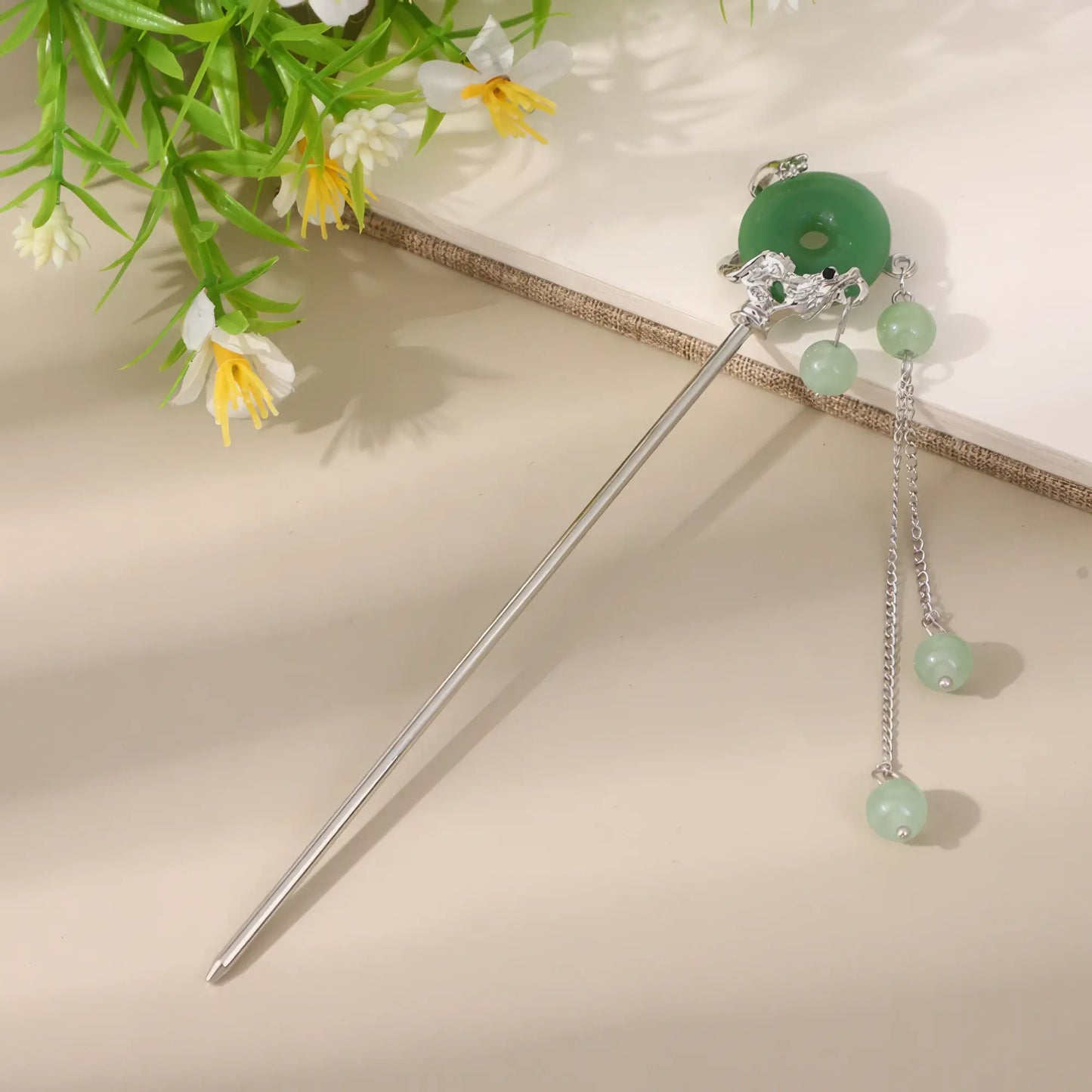 Moyunxuan hairpin, silver with green bead and tassel, on beige background with greenery