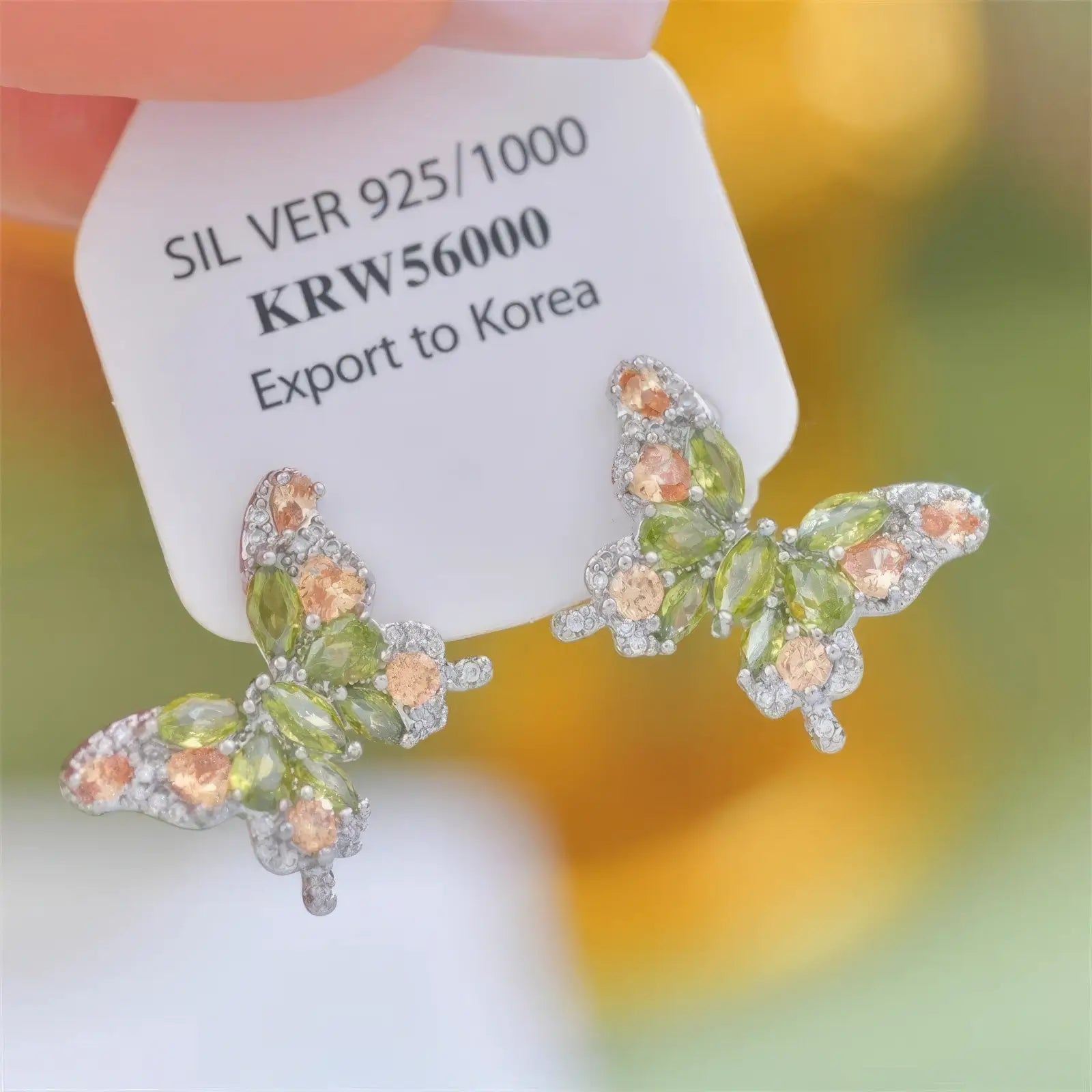 Hand holding orange and green zircon butterfly earrings with a price tag