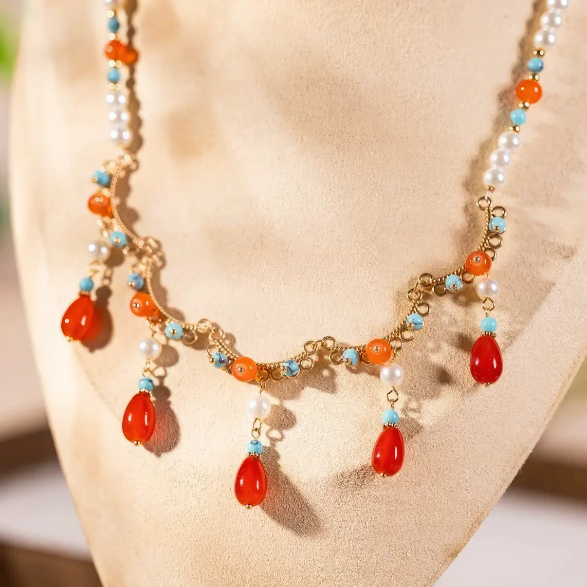 Close - up of orange - red water drop necklace with pearls and colorful beads, displayed on light surface, front view