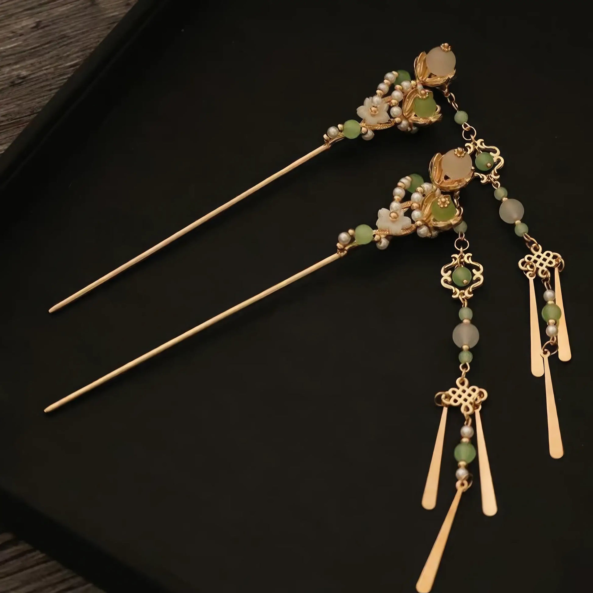 Set of two green jade and gold hairpins with detachable tassels, displayed on a black surface.
