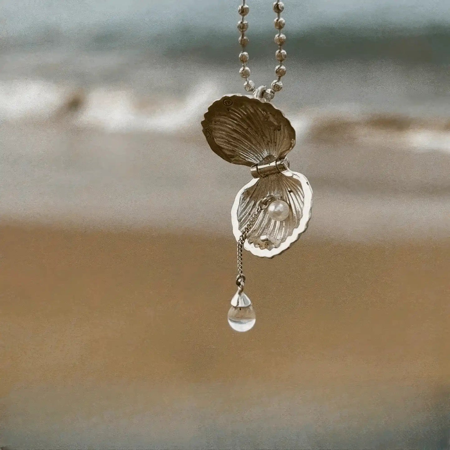 Gold pearl shell pendant necklace displayed on beach, emphasizing seaside theme