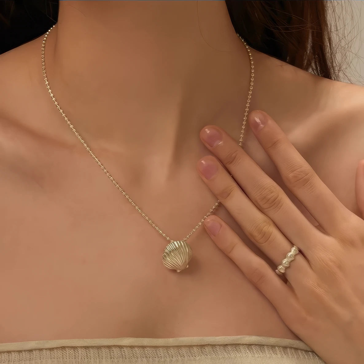 Gold pearl shell pendant necklace worn, with hand gesture, emphasizing beauty