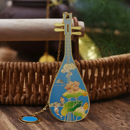 Pipa - shaped bookmark with blue - colored landscape pattern, hanging on a small chain, placed on a woven basket background.