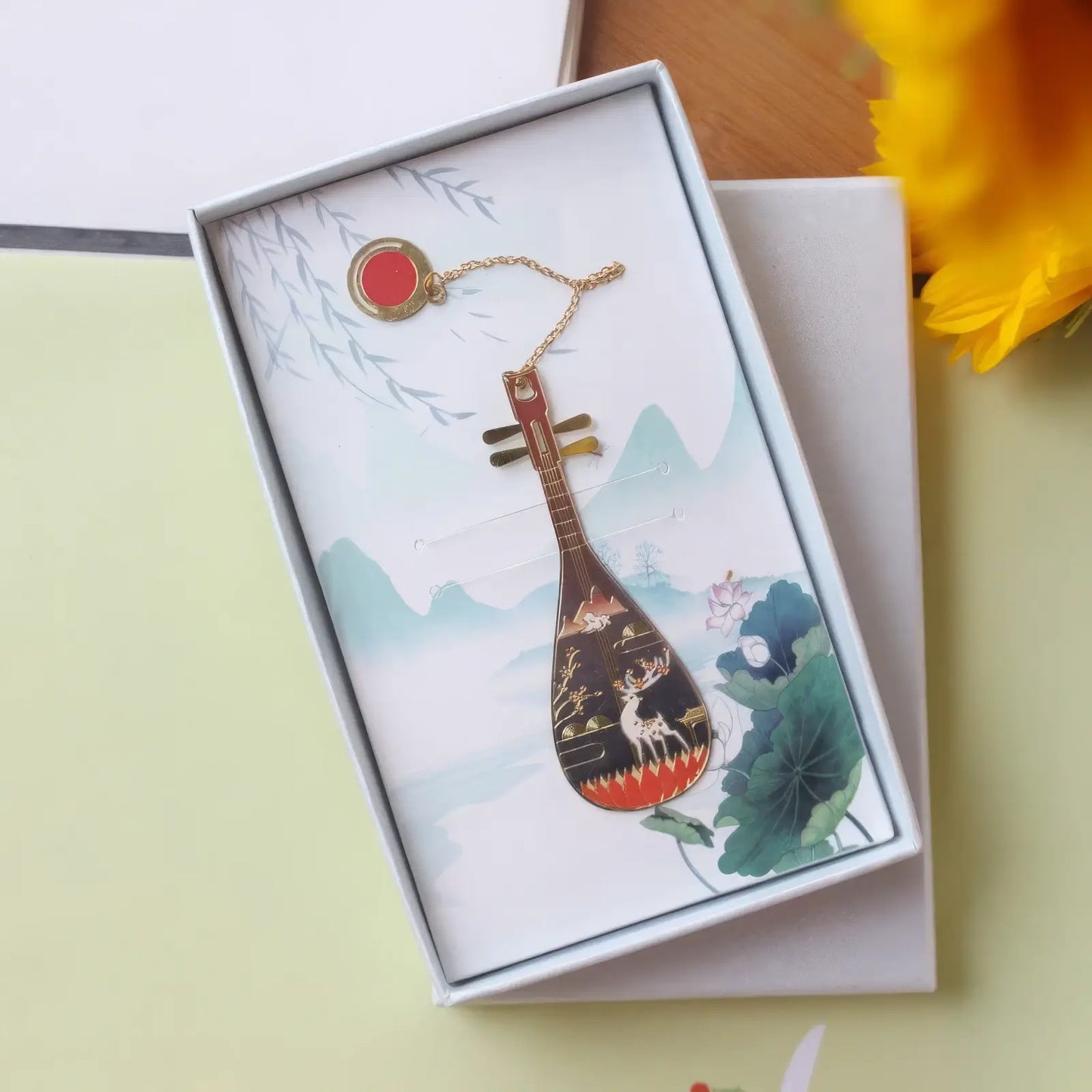Pipa - shaped bookmark of dark color, showcased in a white - bordered box with a landscape pattern, featuring a pendant chain.