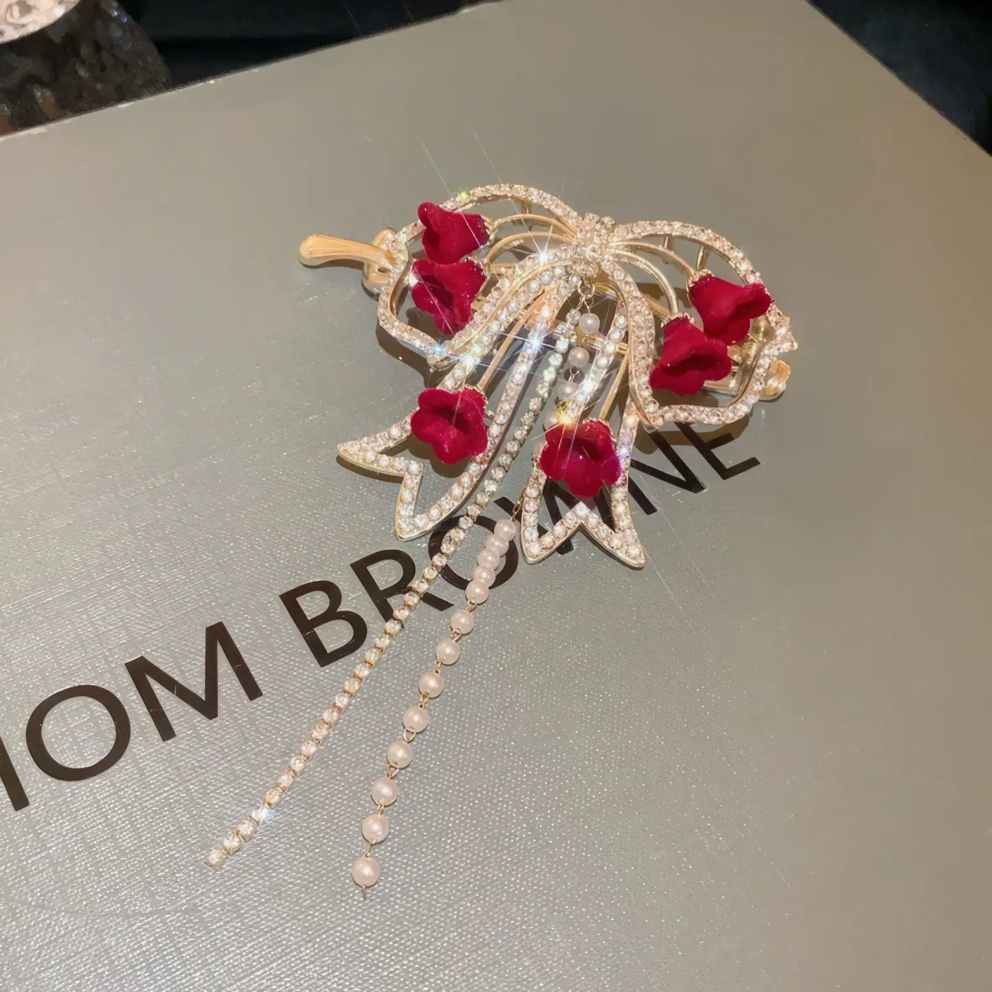 Detailed view of gold - base red flower butterfly hair clip on box