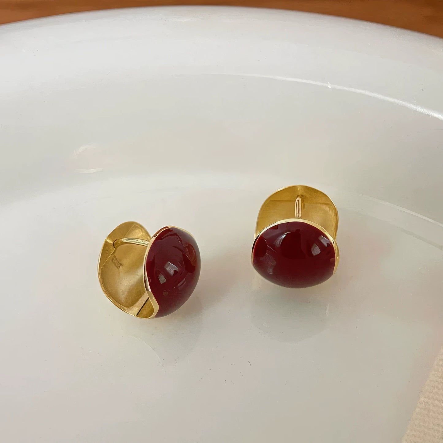Red round ear clips placed on white plate, showing gold backing