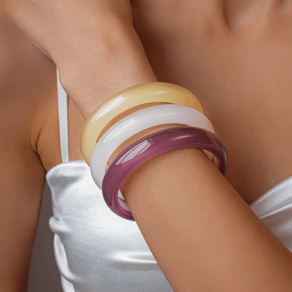 Stack of resin geometric round bangles (yellow, white, purple) worn on wrist, highlighting layering
