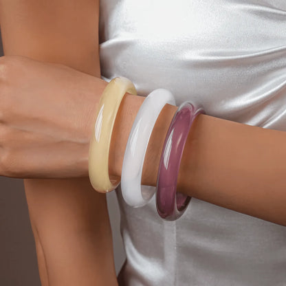 Stack of resin geometric round bangles (yellow, white, purple) worn on wrist, showcasing style