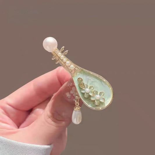 Hand holding rose pipa hair clip, green and gold design with pearl accents