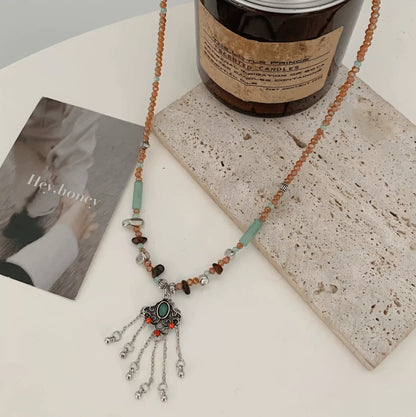 Ruyi tassel lock pendant necklace displayed with a bottle and magazine, showcasing ethnic style