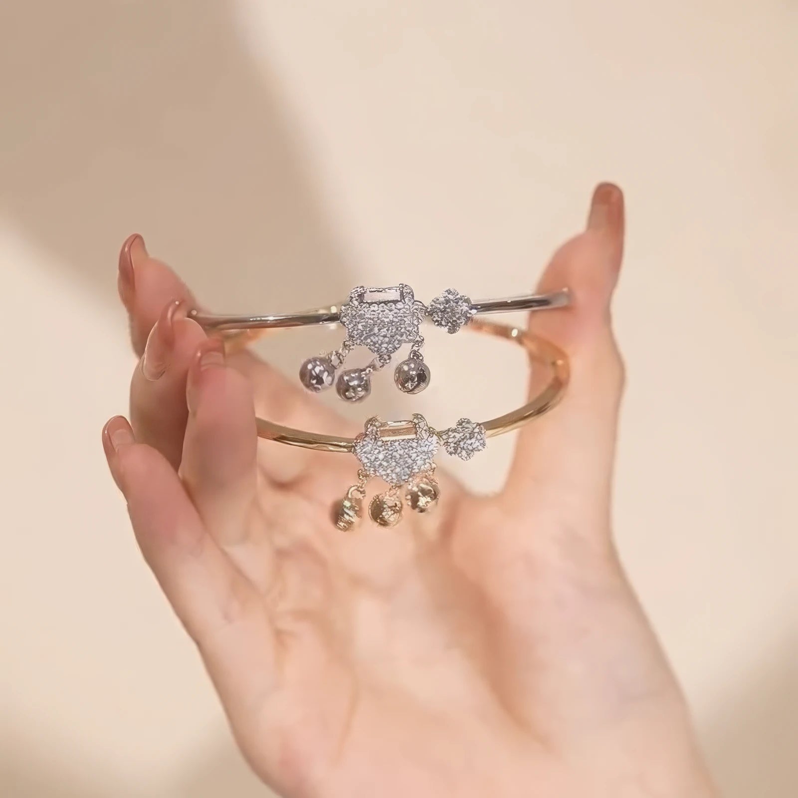 Hands holding silver and gold safety lock bracelets, showcasing design details
