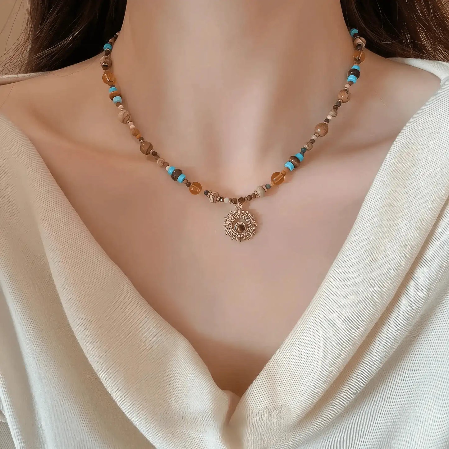 Sunflower beaded necklace, multi - color stones, gold - tone pendant, worn on draped white top