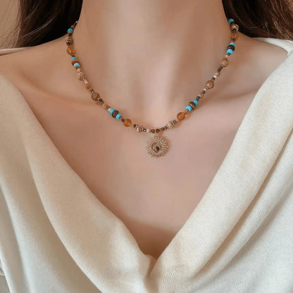 Sunflower beaded necklace, multi - color stones, gold - tone pendant, worn on draped white top