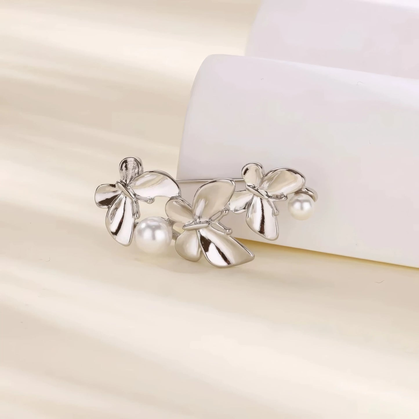 Silver three - butterfly brooch with pearls, displayed on white curved surface, highlighting elegance
