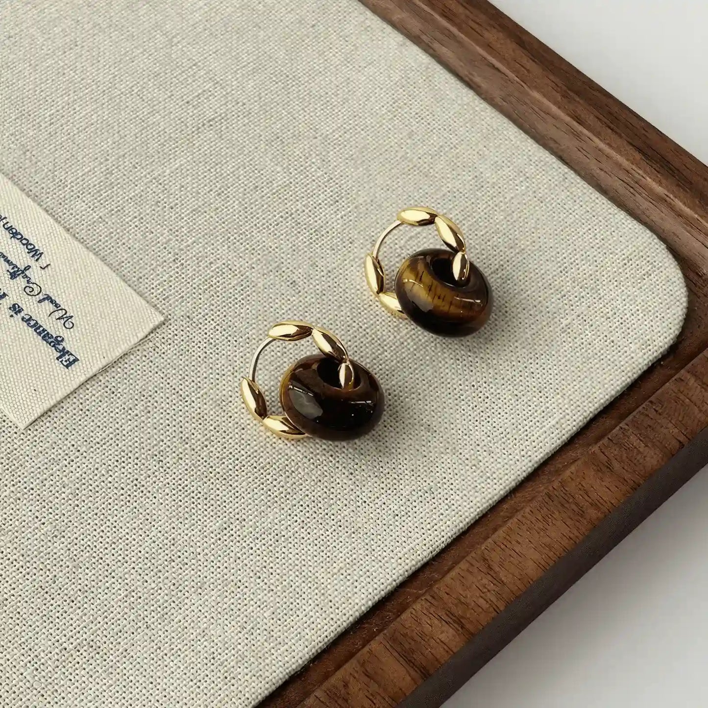 Tiger eye stone hoop earrings, gold - tone, displayed on beige pad with wood trim