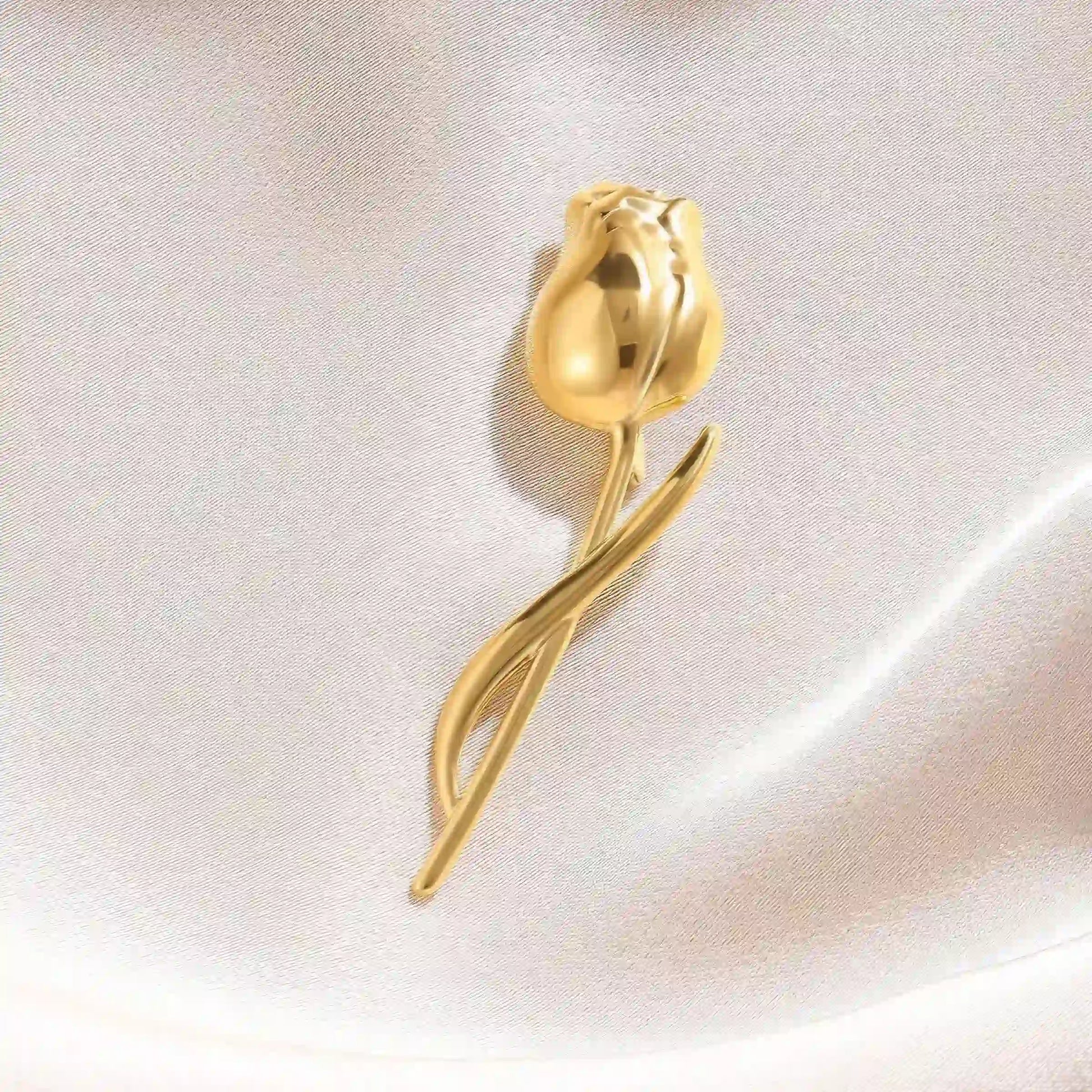 Gold tulip brooch placed on white silk fabric, showcasing elegant design