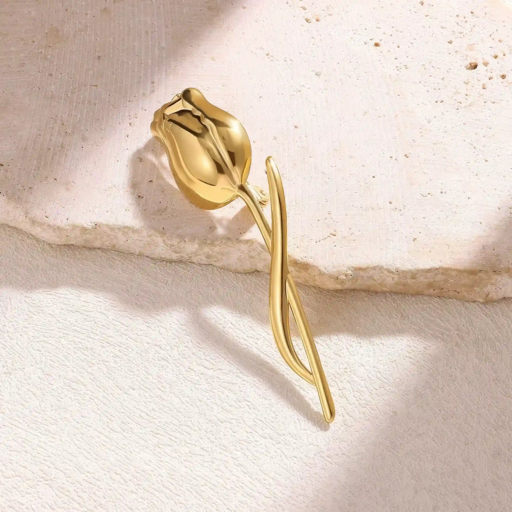 Gold tulip brooch placed on beige stone, side view, highlighting texture