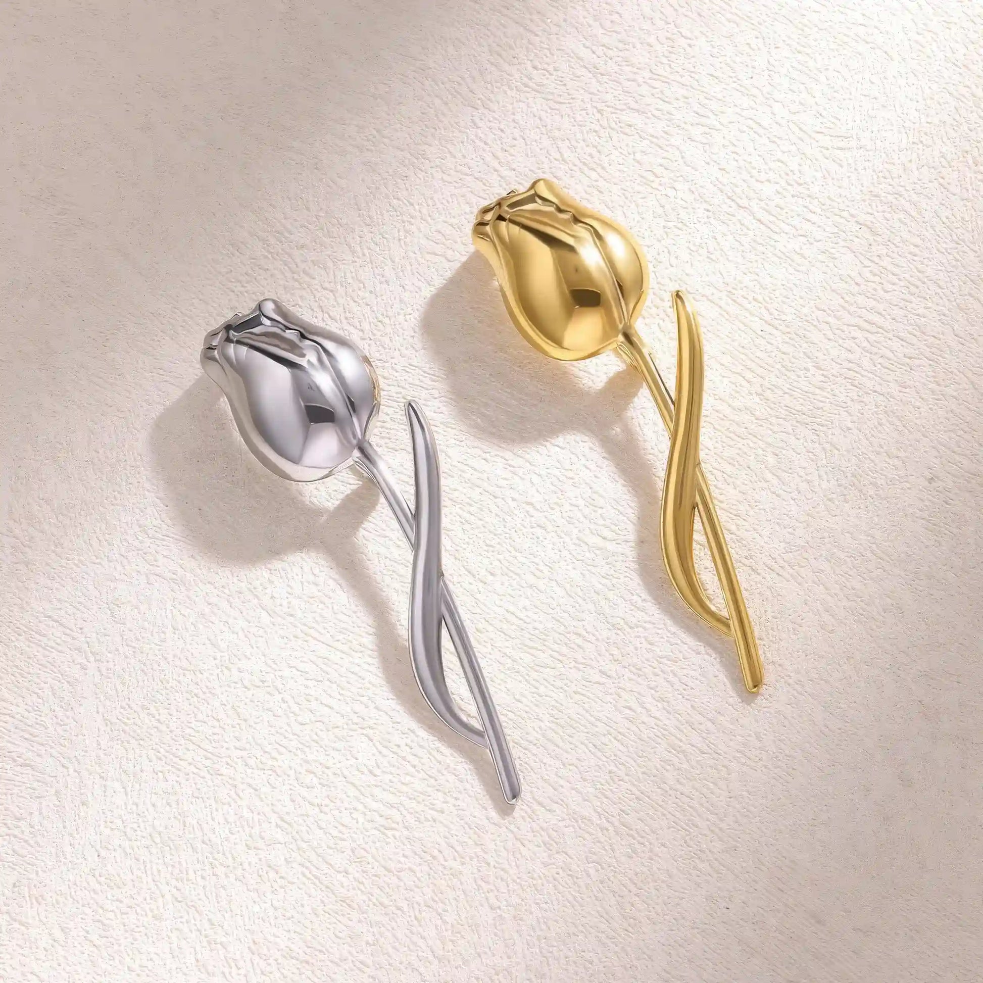 Gold and silver tulip brooches placed on beige stone, showcasing variety