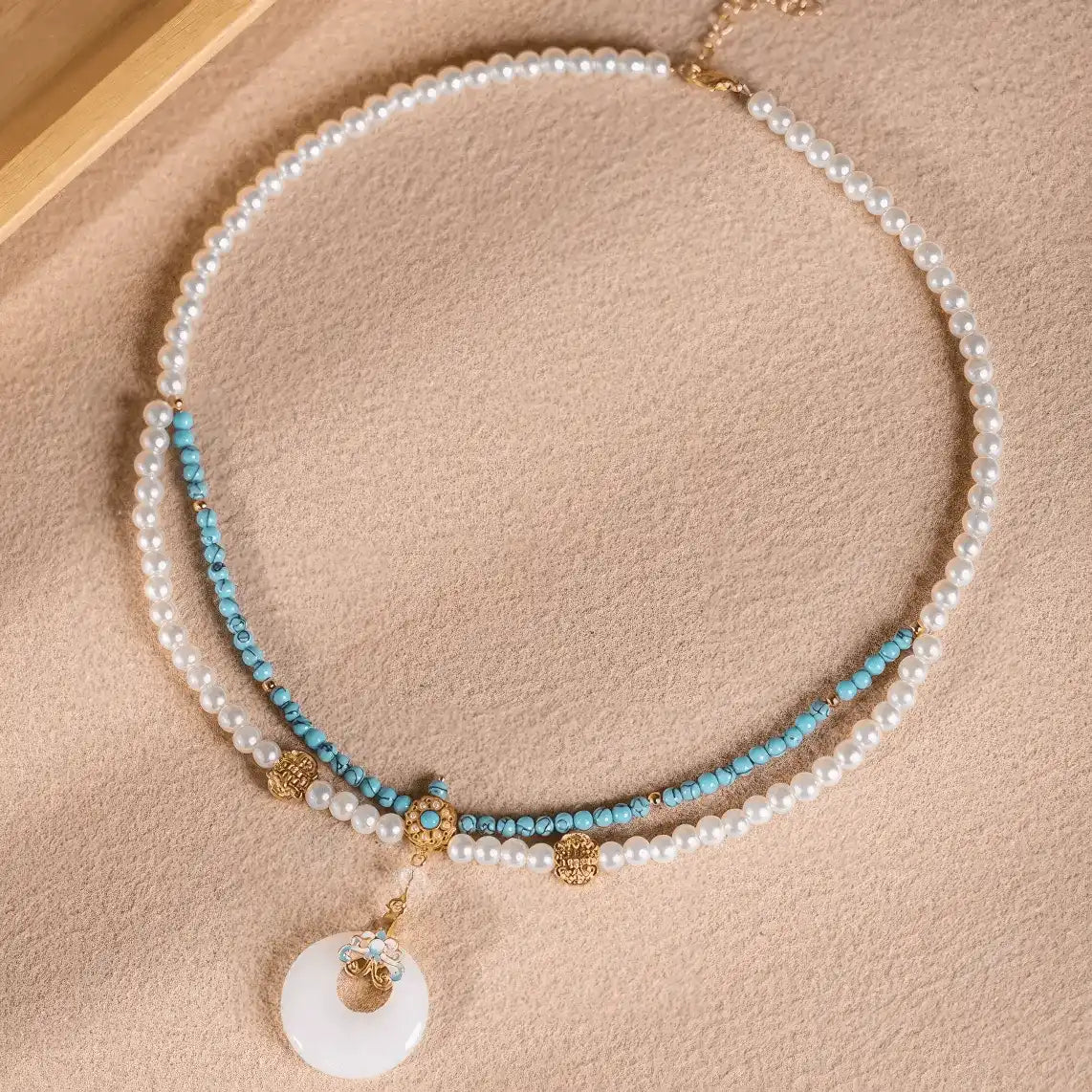 urquoise peace buckle necklace with pearls, displayed on light surface, full view