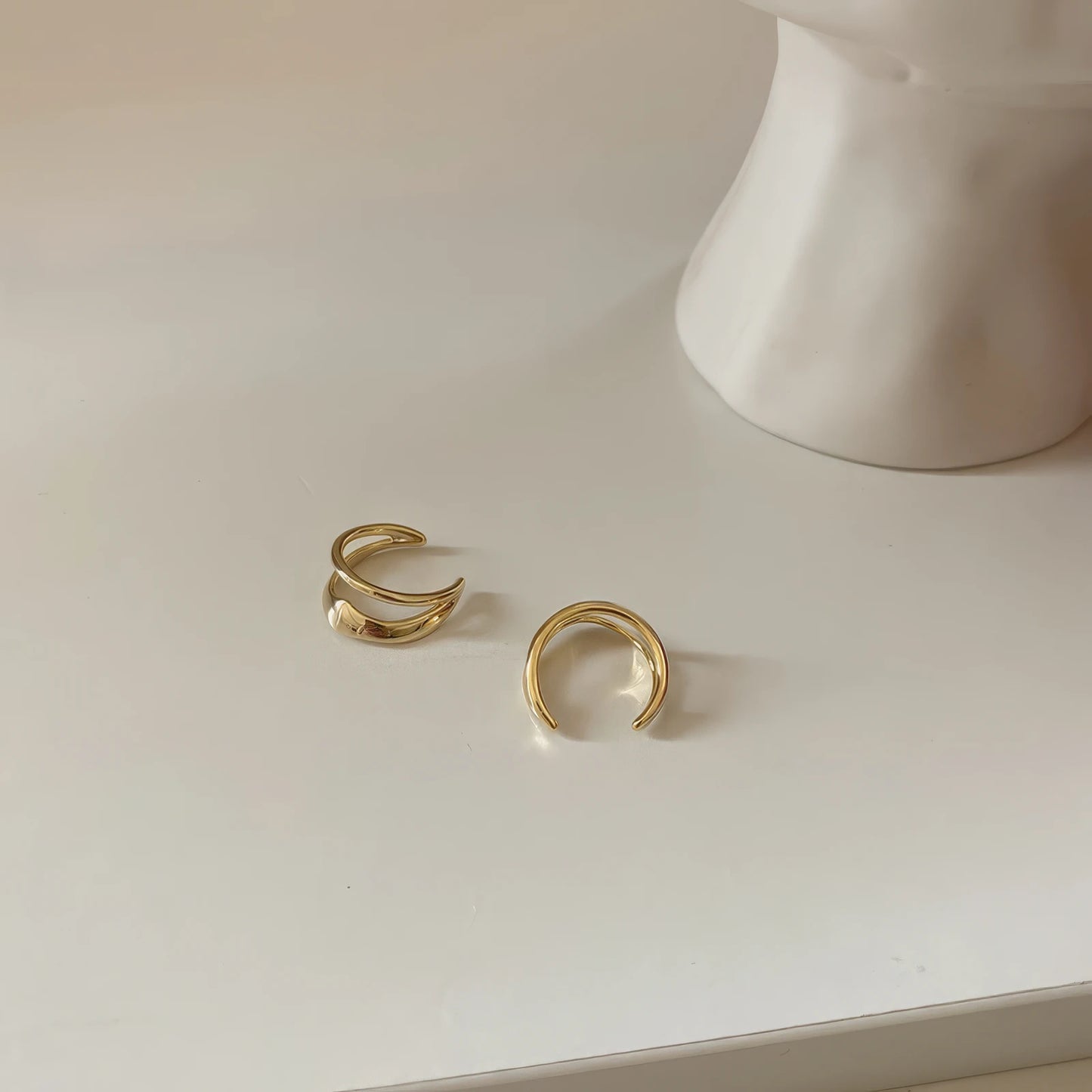 Gold vintage geometric high - end ear cuffs displayed on a white surface, paired with a white object, emphasizing the design
