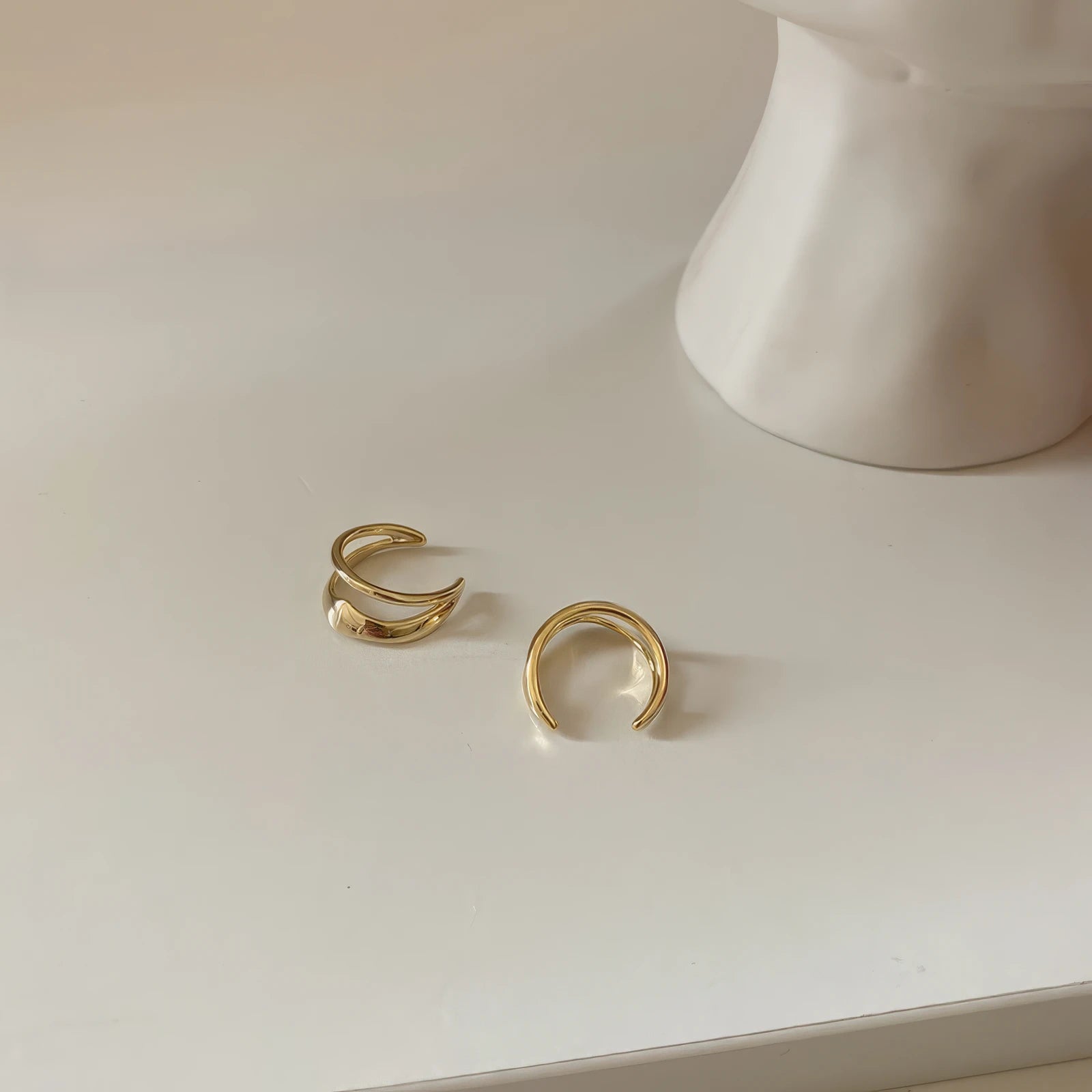 Gold vintage geometric high - end ear cuffs displayed on a white surface, paired with a white object, emphasizing the design
