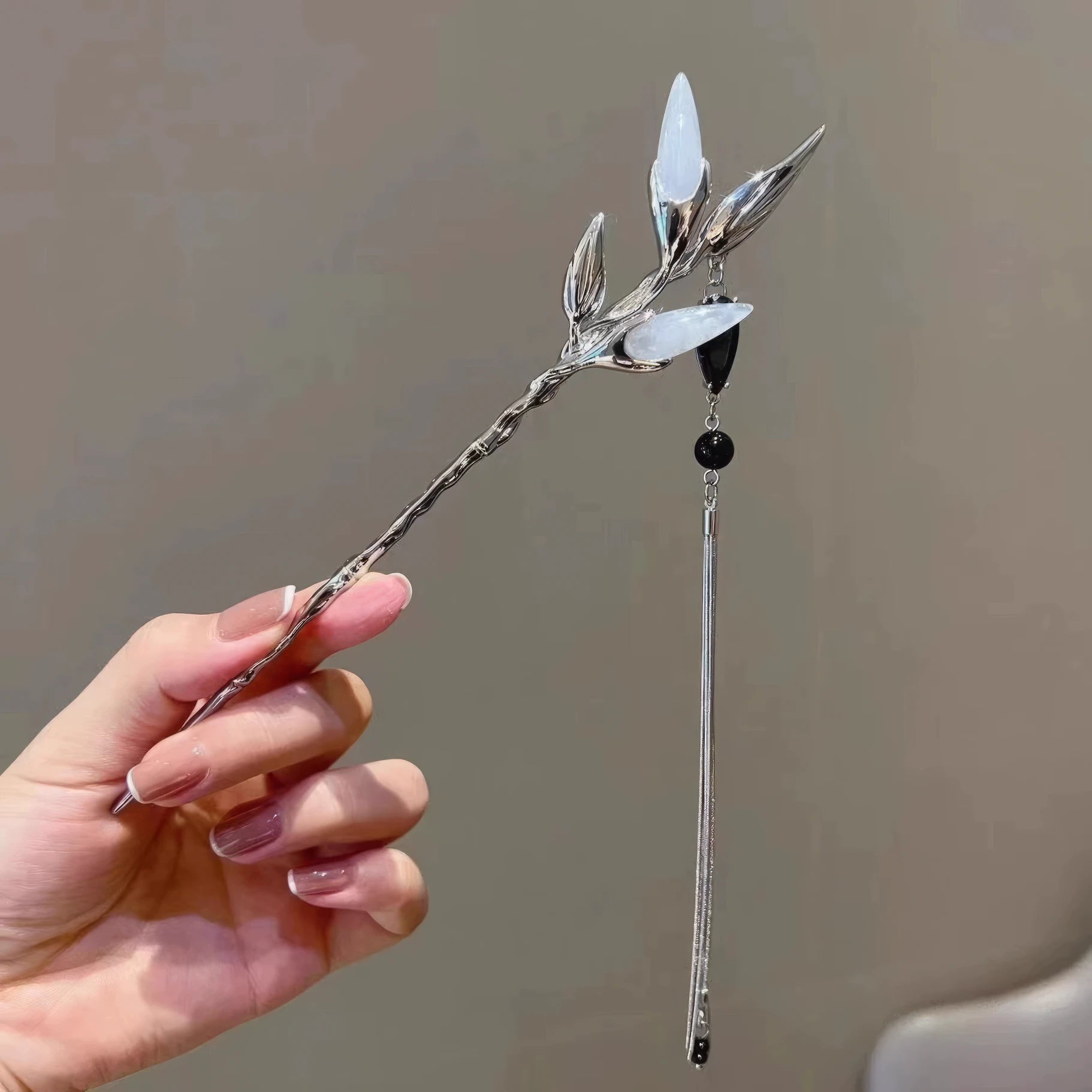 Hand holding silver white jade bamboo tassel hairpin, light background