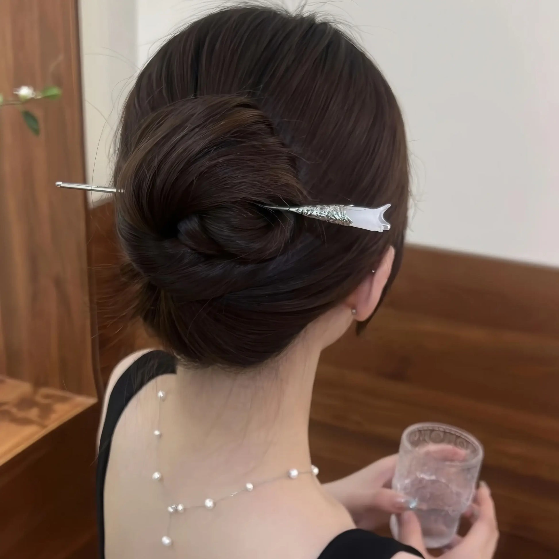 White magnolia hair pin worn in updo, model holding glass, showcasing simplicity