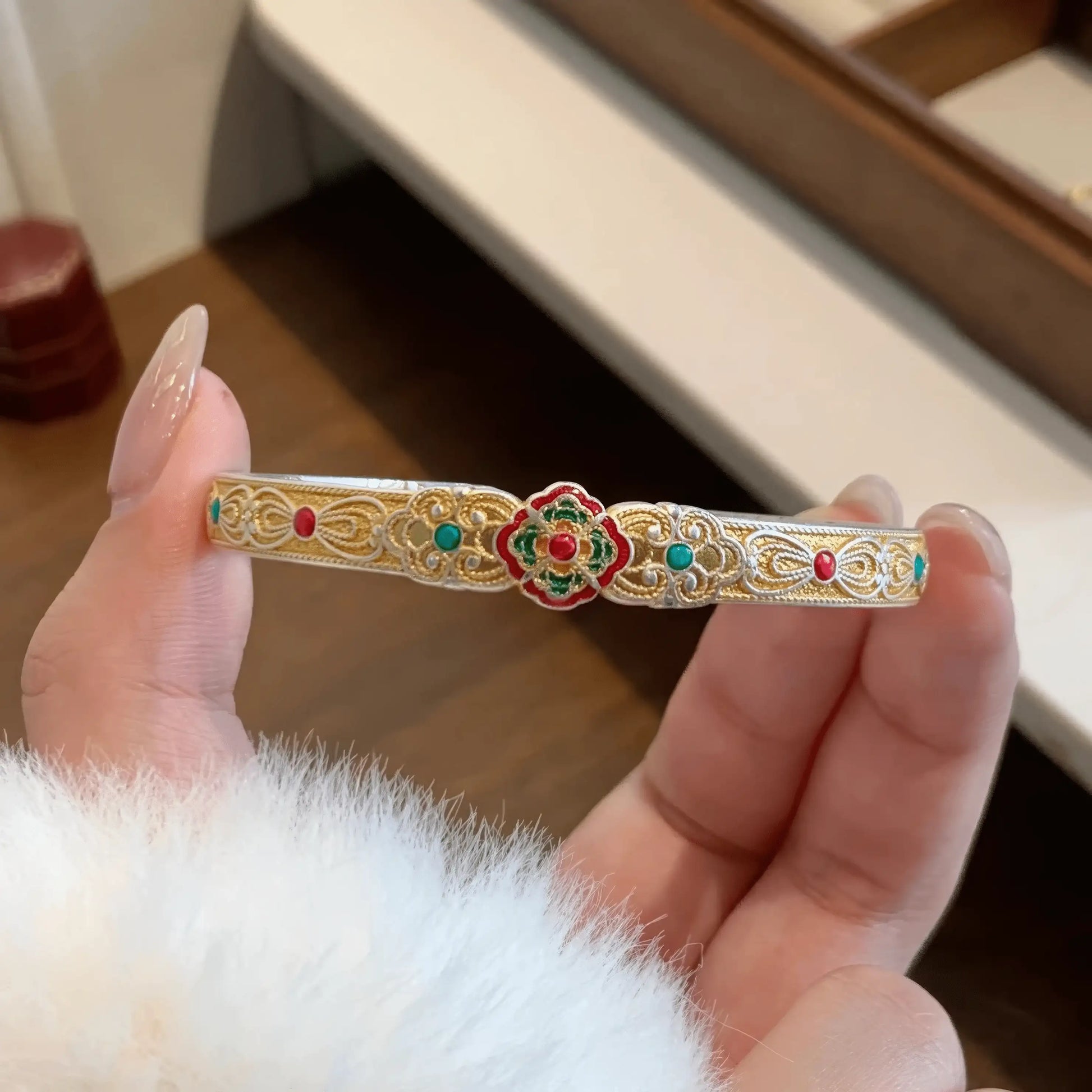 Hand holding gold white orchid bangle, highlighting intricate details