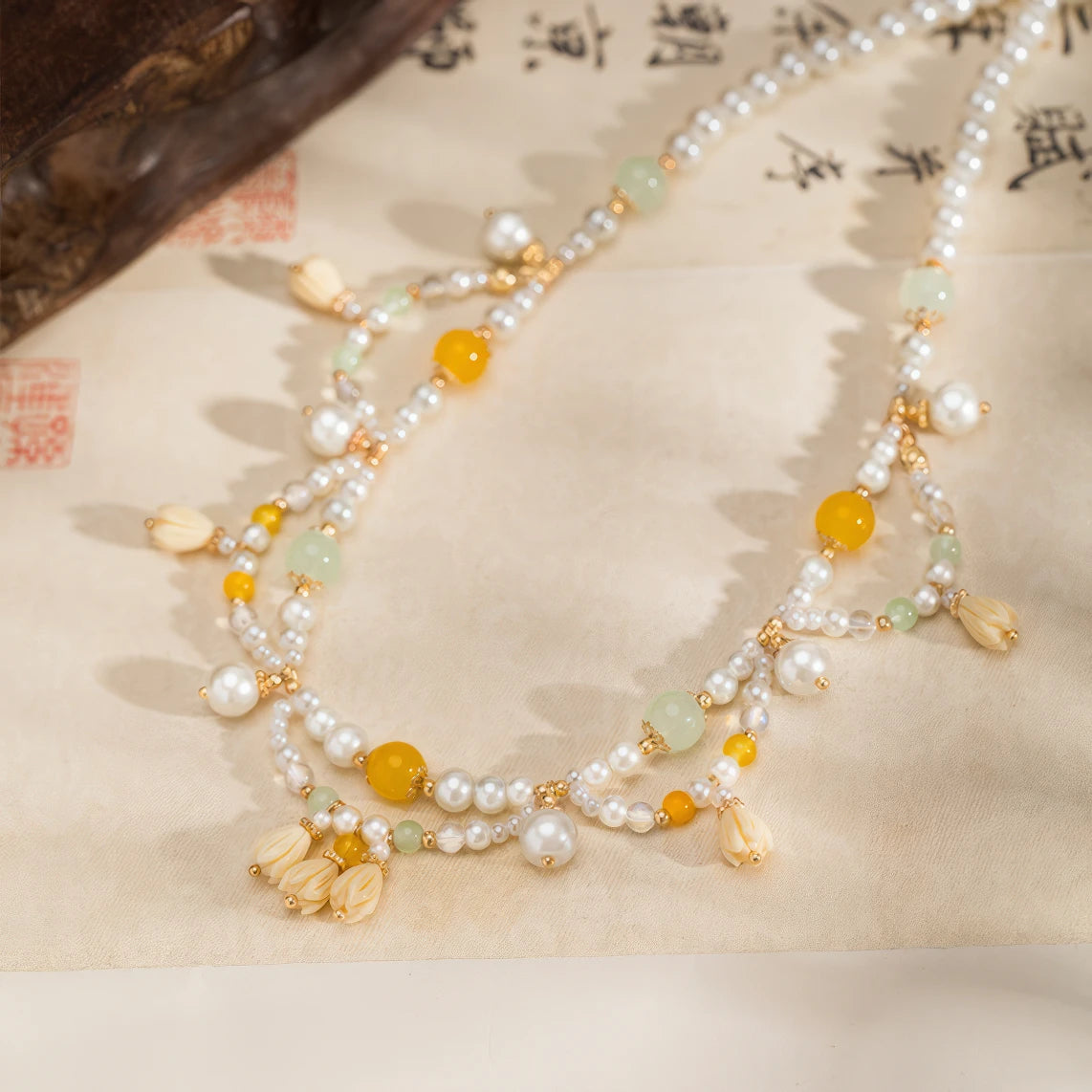 Yellow lily - of - valley necklace with pearls and beads, displayed on calligraphy paper, full view