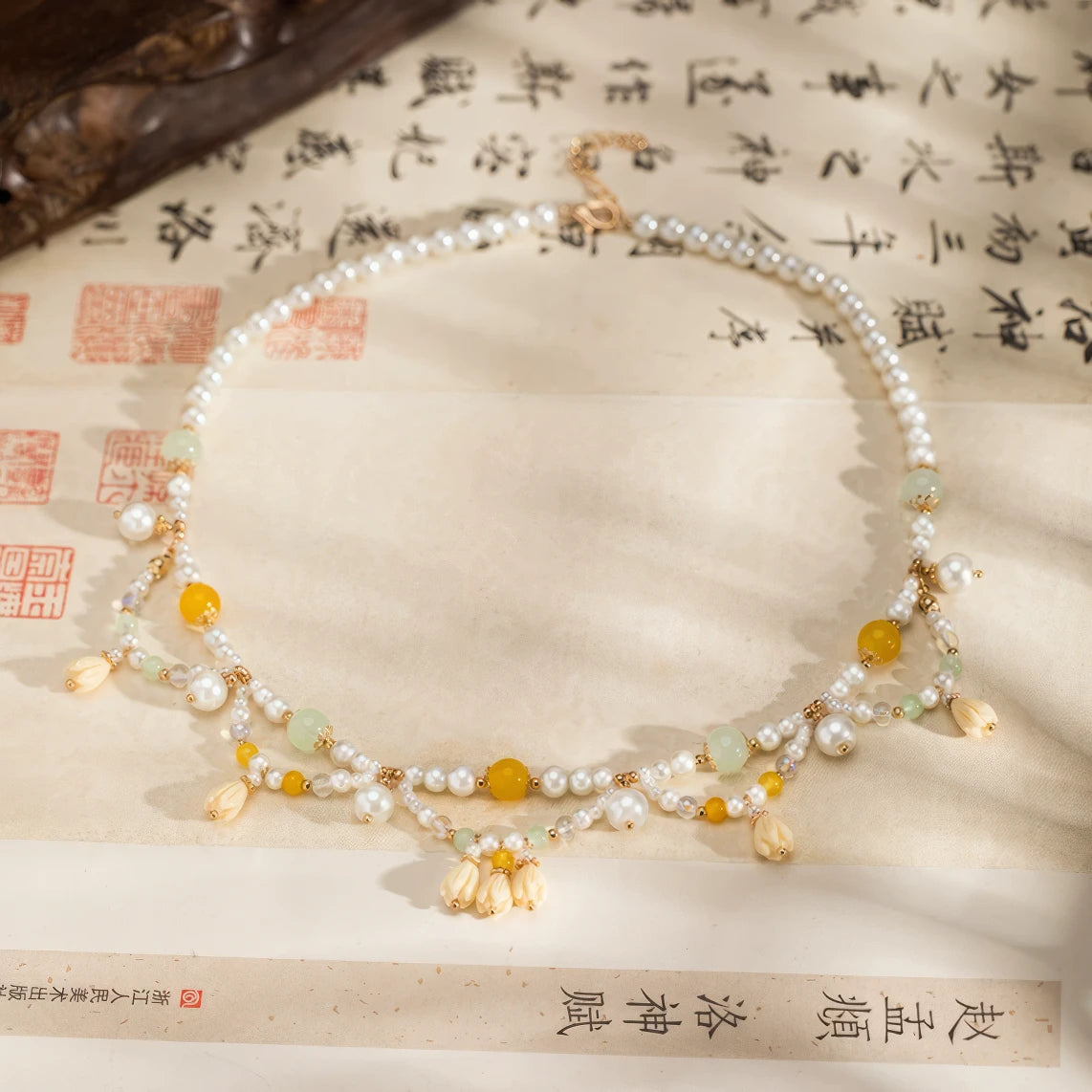 Yellow lily - of - valley necklace with pearls and beads, displayed on calligraphy paper, side view